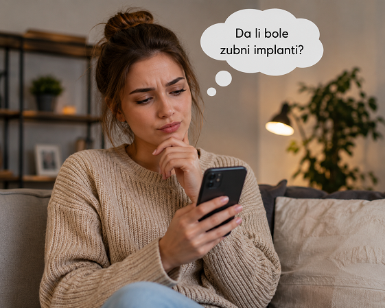 Devojka smedje kose sedi na kaucu i gugla da li bole zubni implanti
